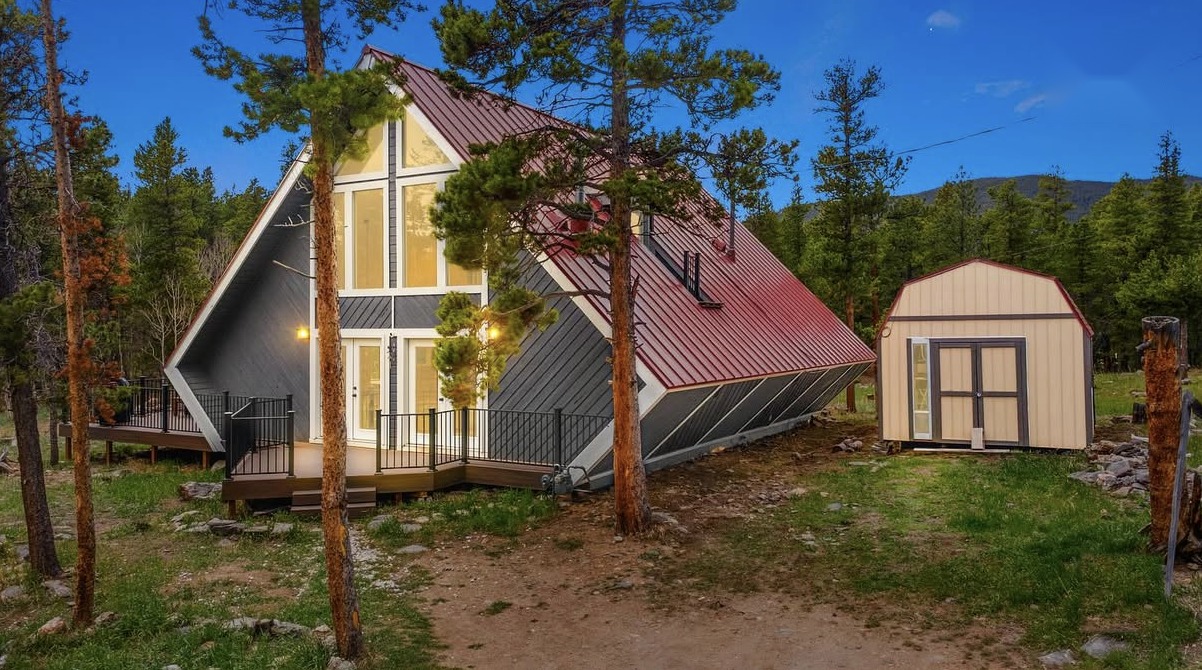 A-frame mountain cabin with a red metal roof and wraparound deck at dusk, Black Hawk, Colorado short-term rental