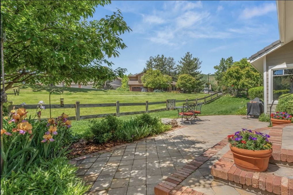 Backyard patio with flower beds and a split-rail fence on open space