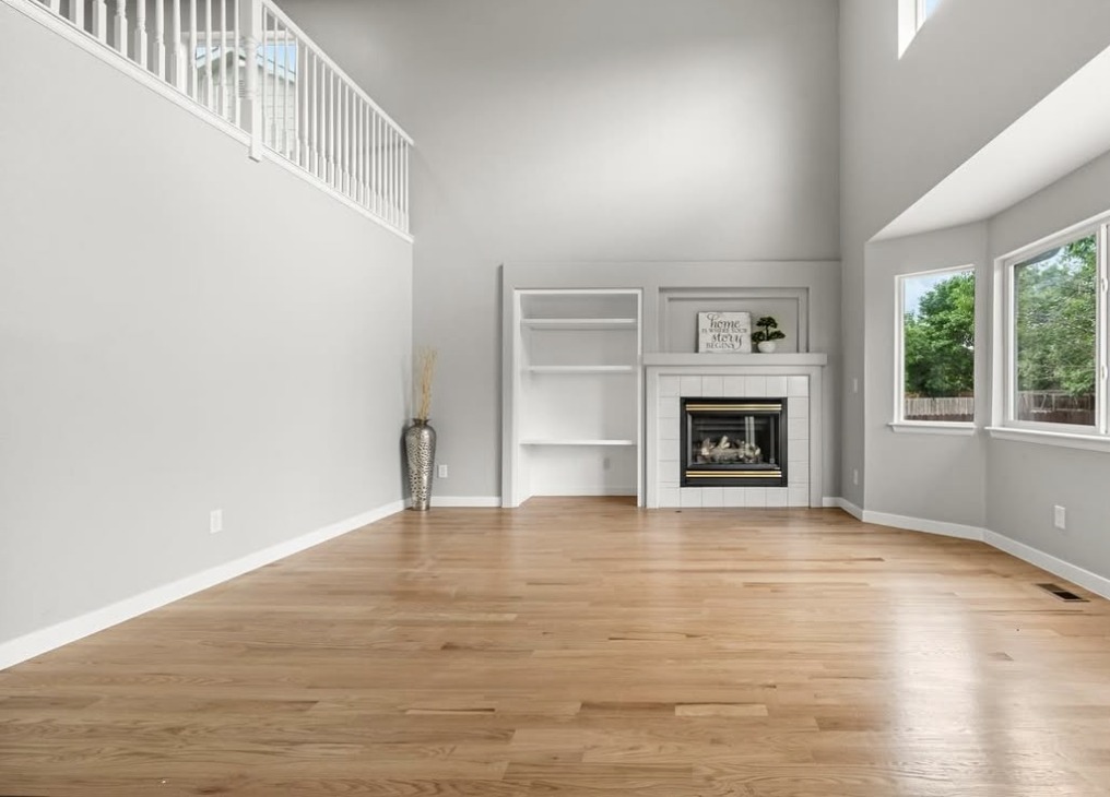 Two-story vacant living room with corner fireplace and hardwood floors