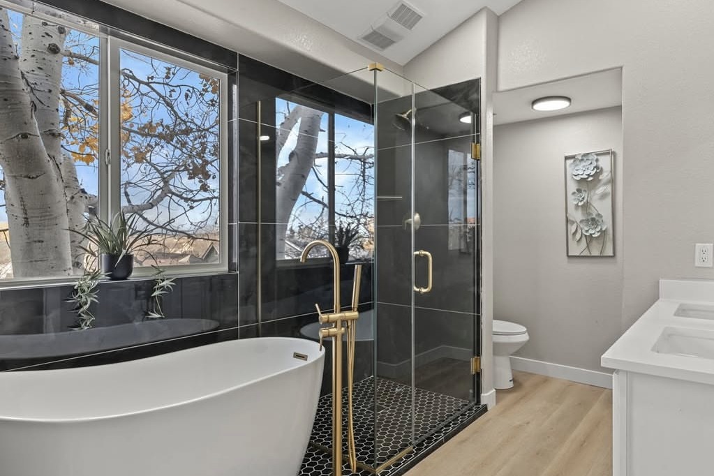 Bathroom with a freestanding tub, gold fixtures and black tile