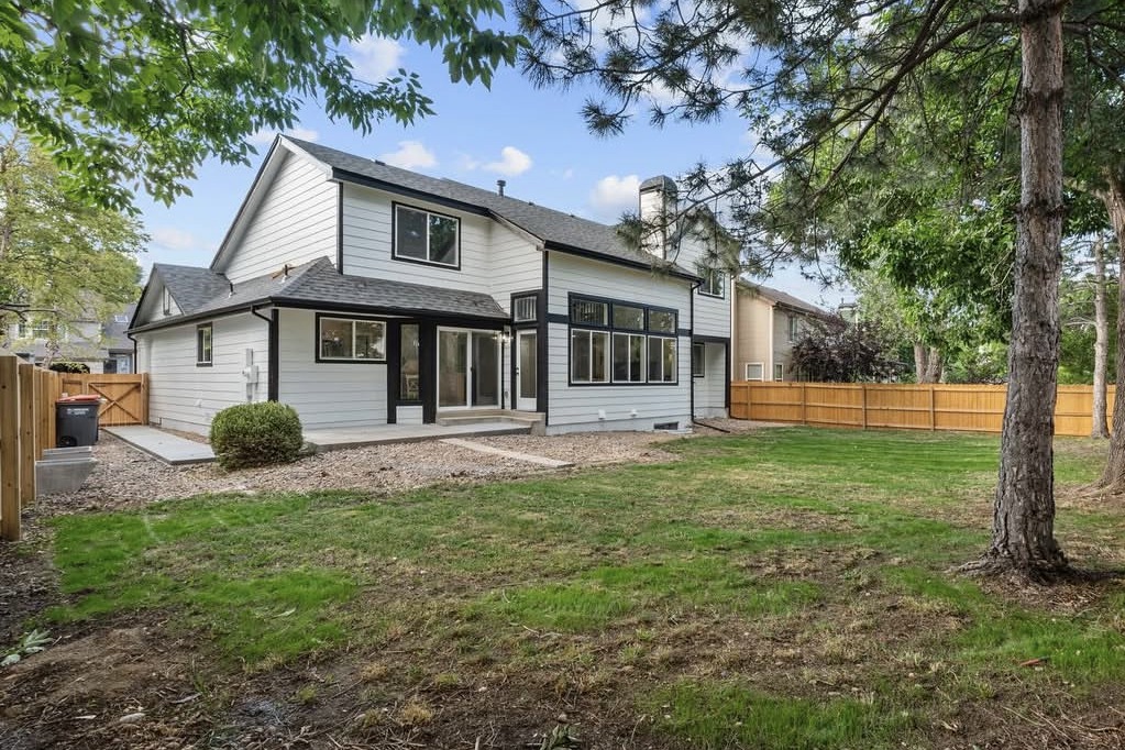 Back of a two-story home with a large grassy yard and pine trees